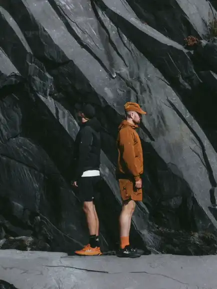 Two men standing against rock wall.